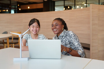 Asian girl student works on science project with an African woman teacher with laptop in...