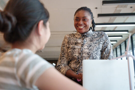 An African woman teacher smiles with an Asian girl student during a science lesson in an international classroom, working together with teamwork and smiling children. - Powered by Adobe