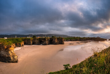 Dramatic sky over As Catedrais beach Galicia Spain iconic rock arches towering above tidal sand at...