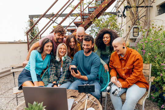 Group of diverse startup founders sharing laughter while creating content on rooftop terrace