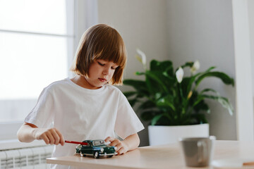 A young boy playing with a toy car, focusing intently while using a red tool. The bright indoor...