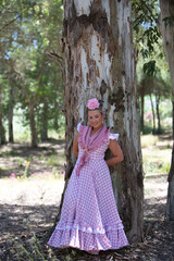 A beautiful young Spanish woman dressed in a traditional pink and white flamenco dress with a...
