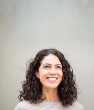 Portrait of a smiling woman with curly hair looking up, standing against wall
