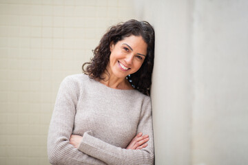 Portrait smiling woman leaning against a wall with arms crossed