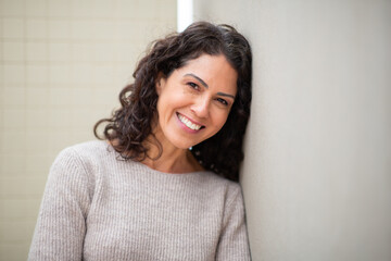 Fototapeta premium Portrait of a smiling woman with curly hair leaning against a light-colored wall