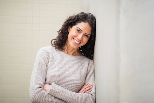 Portrait smiling woman leaning against a wall with arms crossed