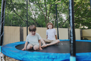 Happy children jumping on a trampoline, enjoying a sunny day outdoors, surrounded by greenery and...