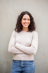 Portrait of a confident woman with curly hair smiling with arms crossed against background