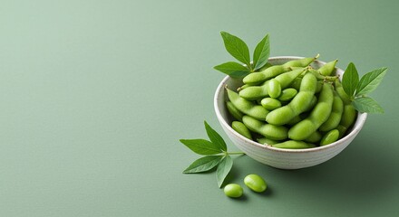Green edamame beans in white bowl with leaves on soft green background