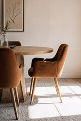 Round oak table and cinnamon fabric chairs bathed in soft afternoon sunlight