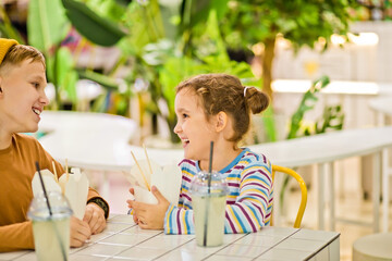 Kids child boy and girl eating ramen noodle wok with chopsticks in food court. Lunch time.
