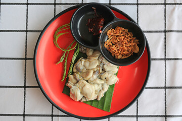 Oysters serve with spicy sauce and fried garlic in red-black plate on the table. Top view.