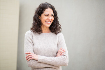 Portrait of a cheerful woman with arms crossed, looking away and smiling, dressed casually outdoors