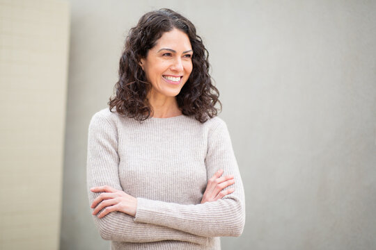 Portrait of a cheerful woman with arms crossed, looking away and smiling, dressed casually outdoors