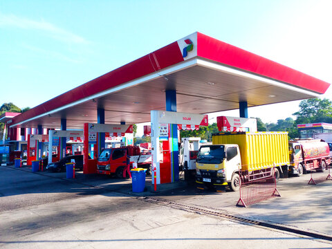 Multiple trucks refueling at Pertamina gas station on a sunny day. Bright red and white canopy with fuel pumps labeled for different services. On September 27, 2024 in West Java, Indonesia.