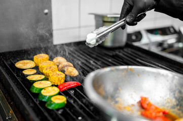 Chef grilling assorted vegetables including zucchini, corn, and mushrooms on a hot grill with...