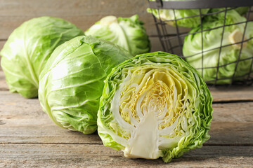 Fresh cabbages and basket on wooden table, closeup