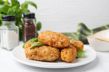 Tasty fried croquettes and basil on white tiled table, closeup