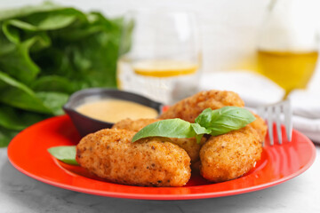 Tasty fried croquettes, basil and sauce on white marble table, closeup