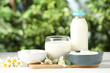 Different fresh dairy products and flowers on white wooden table outdoors