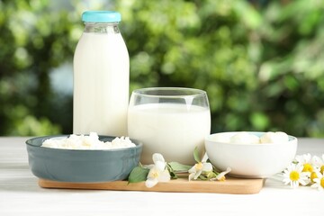 Different fresh dairy products and flowers on white wooden table outdoors