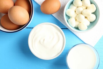Different dairy products and eggs on light blue wooden table, flat lay