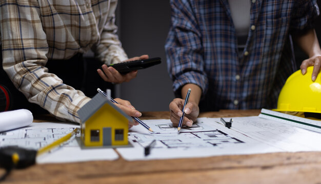 Collaboration female architects brainstorming discuss construction project design blueprints on wooden table in dark office. Colleagues are planning and calculating the budget for house construction.