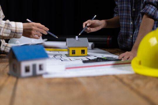 Collaboration female architects brainstorming discuss construction project design blueprints on wooden table in dark office. Colleagues are planning and calculating the budget for house construction. - Powered by Adobe
