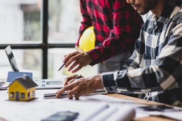 Architect using ruler and pencil reviewing blueprint of architectural project. Two architects are...