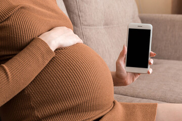 pregnancy with modern technologies.Pregnant woman showing cellphone with empty displayon sofa at...