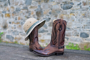 Cowboy boots hat against stone wall background.