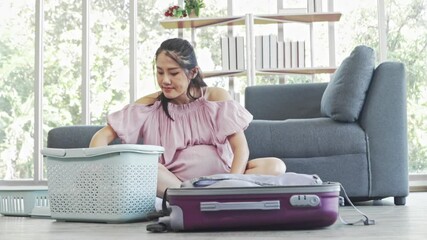 Happy pregnant woman sitting packing clothes and necessities into suitcase to prepare plans and notes in diary for hospital stay in anticipation of delivery and after delivery.