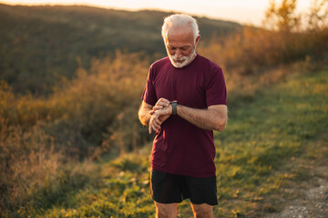 Senior Man Checking Fitness Tracker Outdoors During Sunset