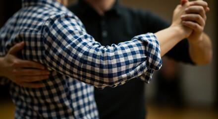 Close up of two people dancing with their arms intertwined; one dancer is wearing a blue checkered shirt.