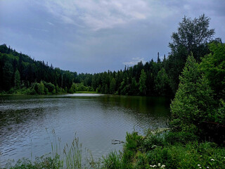 Serene lake surrounded by lush forest under a cloudy sky in the early evening