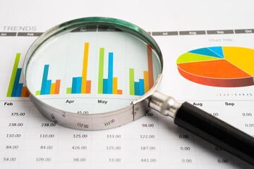 Magnifying glass on data business graphs paper.