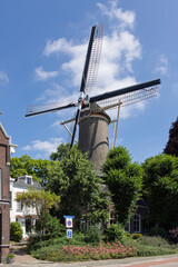 Historic Dutch windmill in Gouda stands tall amidst green trees and buildings, a classic symbol of the Netherlands under a blue sky