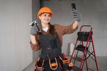 Female builder in safety helmet taking selfie with smartphone holding stapler during home renovation