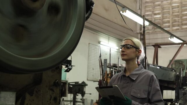 Female lathe operator wearing safety glasses to protect from metal chips while carefully operating metal stamping machine working on thin sheet metal in parts manufacturing plant.