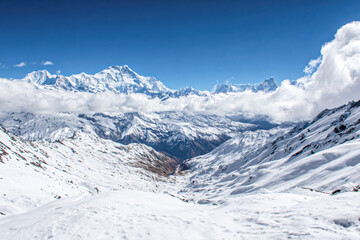 Fototapeta premium Snow-covered mountain range under a bright blue sky with scattered clouds and a valley below.