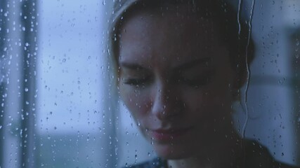 young adult unhappy woman crying standing looking at window rain drops falling water drip flow down the glass, mood depression sadness emotion. sad tears grief grief face eyes. lonely lady, dark room