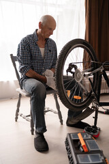 Senior man in shirt repairing bicycle at home. DIY bicycle repair and maintenance
