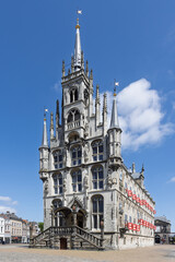 Fototapeta premium Stunning Gothic Town Hall of Gouda, Netherlands, adorned with red flags under a clear blue sky, a true architectural masterpiece.