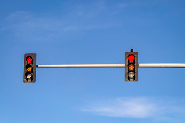 Two red traffic lights hang on a horizontal pole against a vibrant blue sky on a clear day in the...