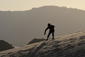 silhouette of a man riding a sandboard down a dune