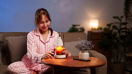 A contented Asian adult female enhances her restful evening with an aromatic candle for a sense of calm and wellness at home