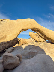 Scenic view of famous Arch Rock formation at Joshua Tree National Park, California, United States in warm lights at sunset against blue sky