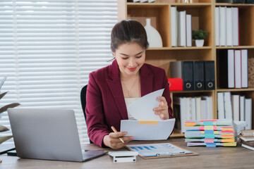 Diligent Review: A focused business woman meticulously examines documents in her modern office, a...
