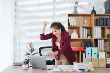 Successful Businesswoman Celebrating: A joyful businesswoman celebrates a success at her desk,...