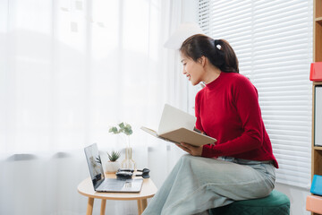 Reading and Connecting: A woman immersed in a book and video call from her cozy home. Capturing...